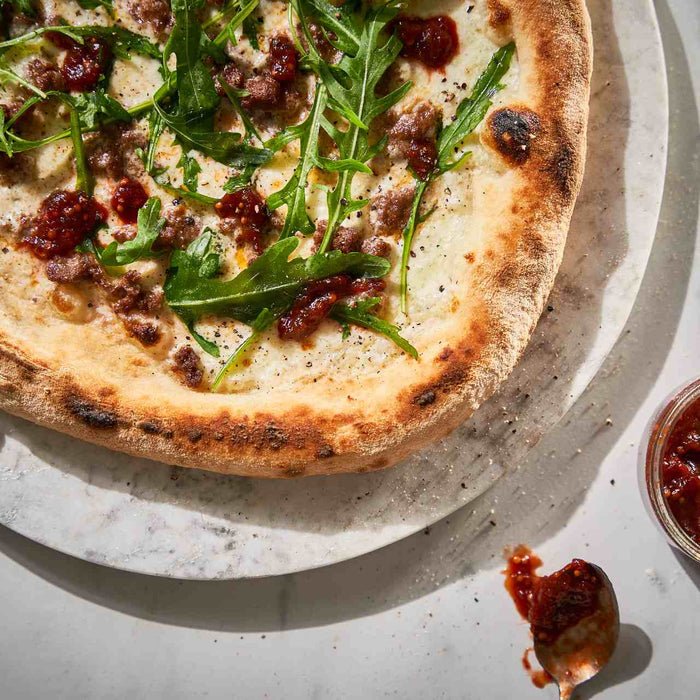 Cooked bratwurst pizza with rhubarb chutney and arugula on a plate next to a small dish of rhubarb chutney.