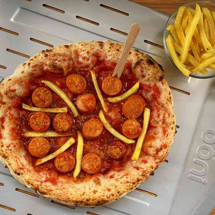 A pizza topped with bratwurst, french fries and German curry sauce on a perforated pizza peel