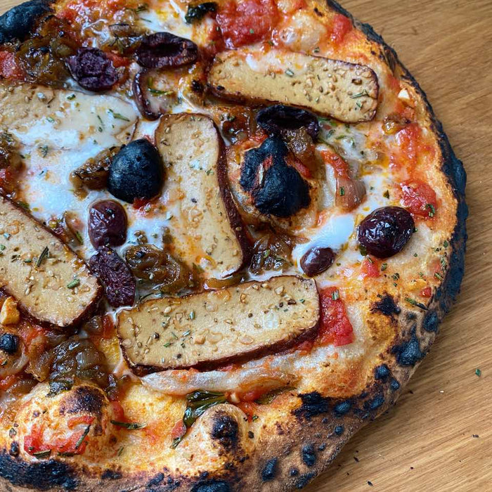 Pizza topped with slices of smoked tofu, caramelised onions, black olives and melted vegan cheddar 