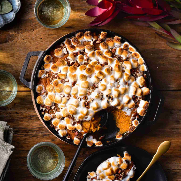Cast iron pan filled with a marshmallow and pecan-topped sweet potato casserole