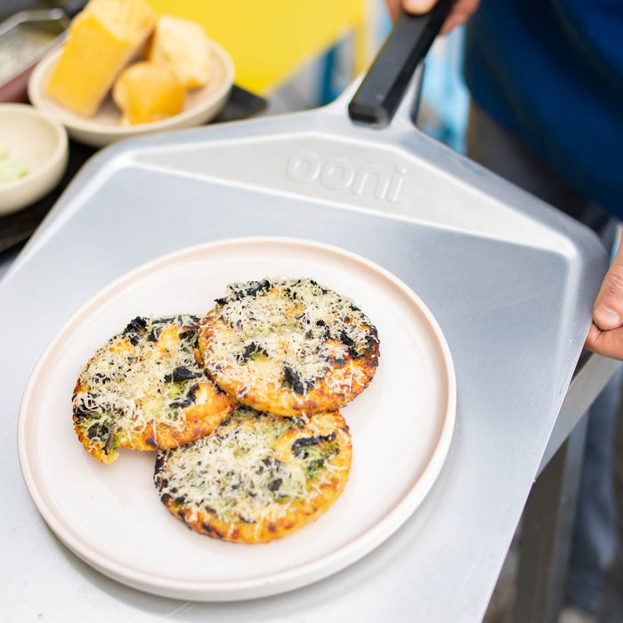 Potato flatbreads covered with garlic butter, cheese and kale on a steel pizza peel