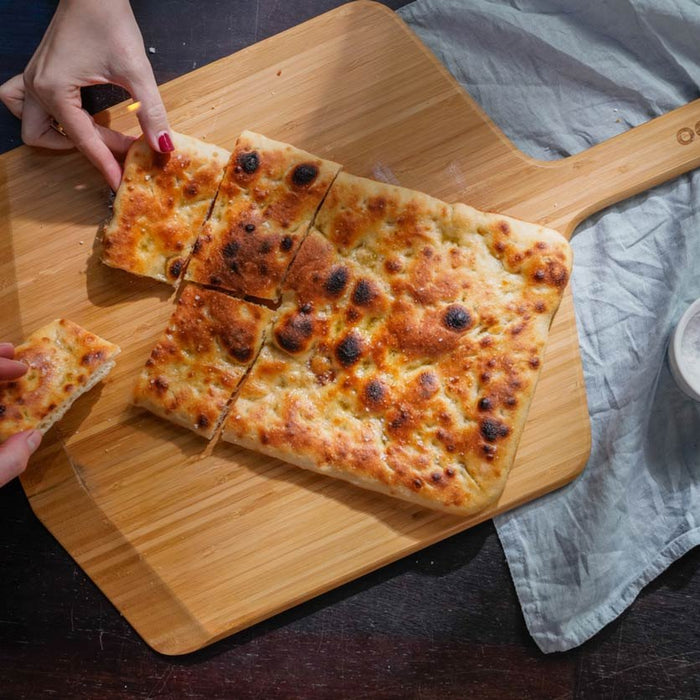 Two hands holding pieces of Roman pizza on an Ooni Bamboo Pizza Peel & Serving Board.