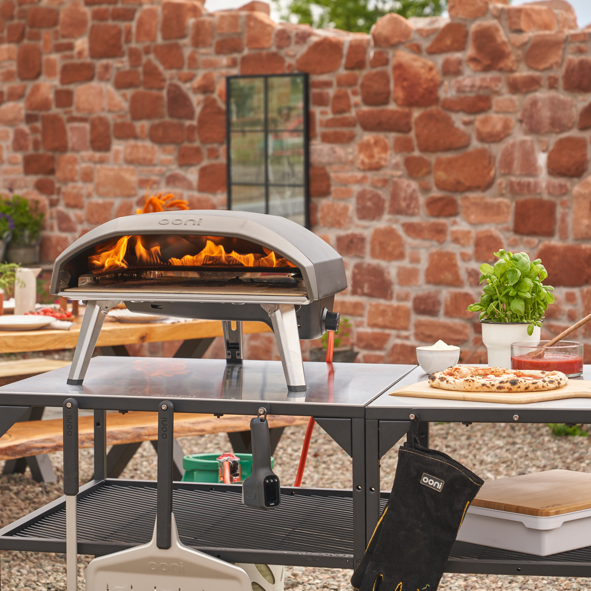 Ooni koda 16 Gas Powered Pizza oven ontop of a modular table with stone brick wall in the background. 