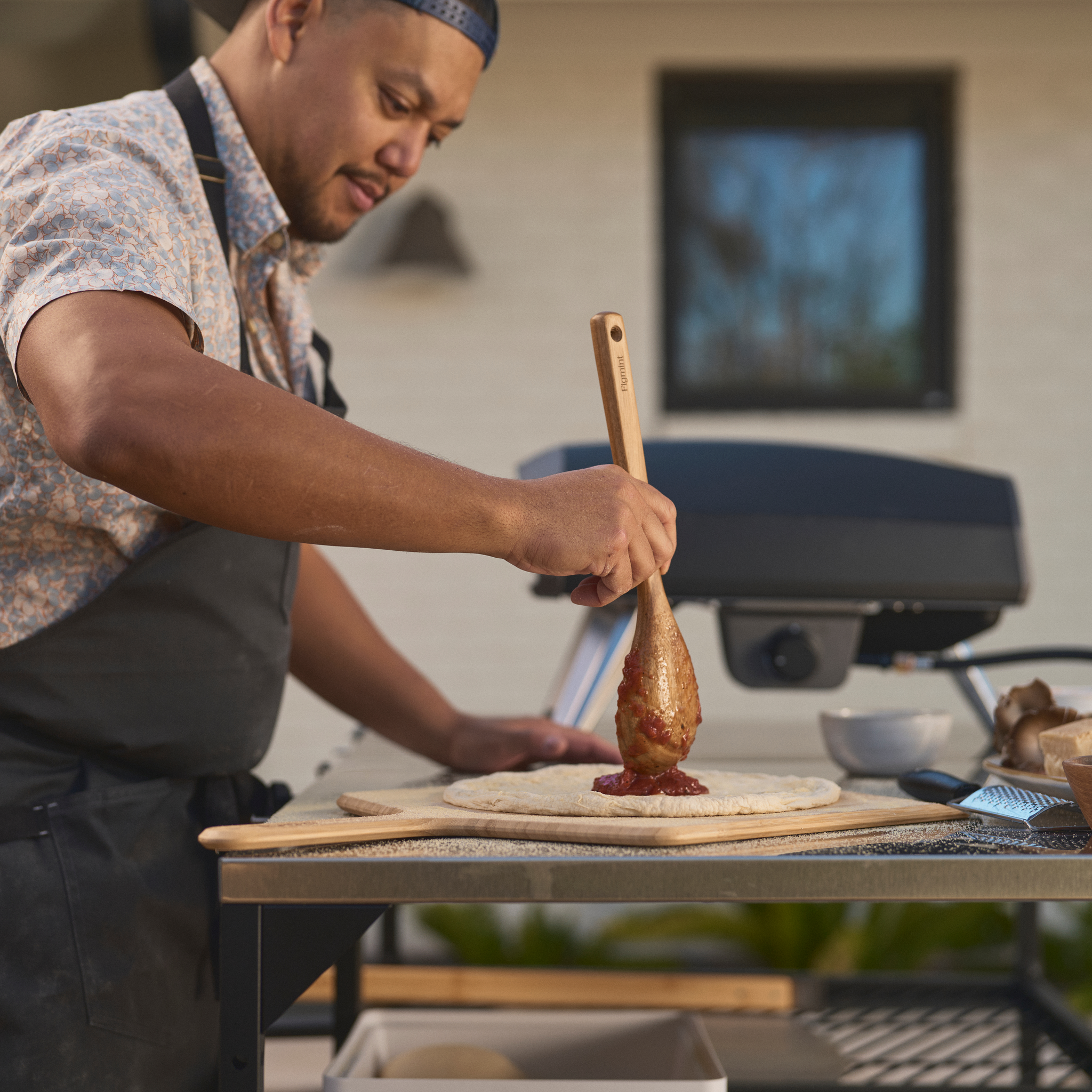 person adding sauce to pizza base in front of the koda 2 pizza oven. 