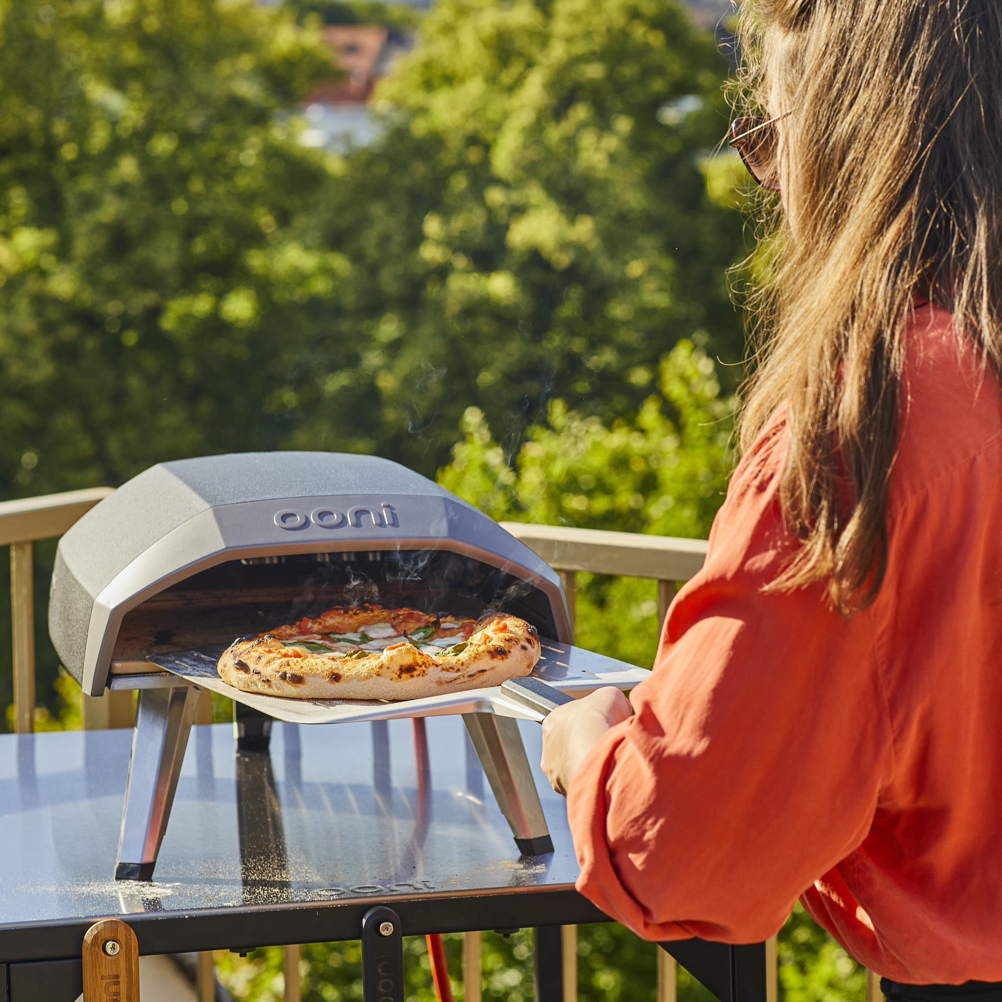 person removing a pizza from the Ooni koda 12 gas powered pizza oven