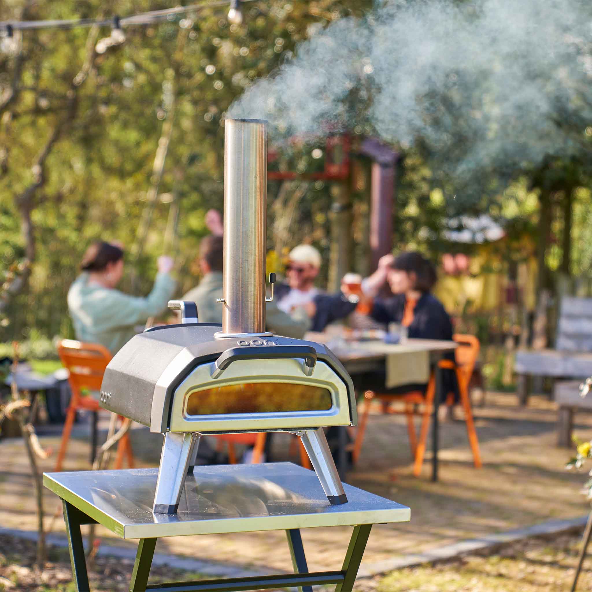 Ooni Karu 2 multi-fuel pizza oven on ooni folding table with smoke appearing from chimney. 