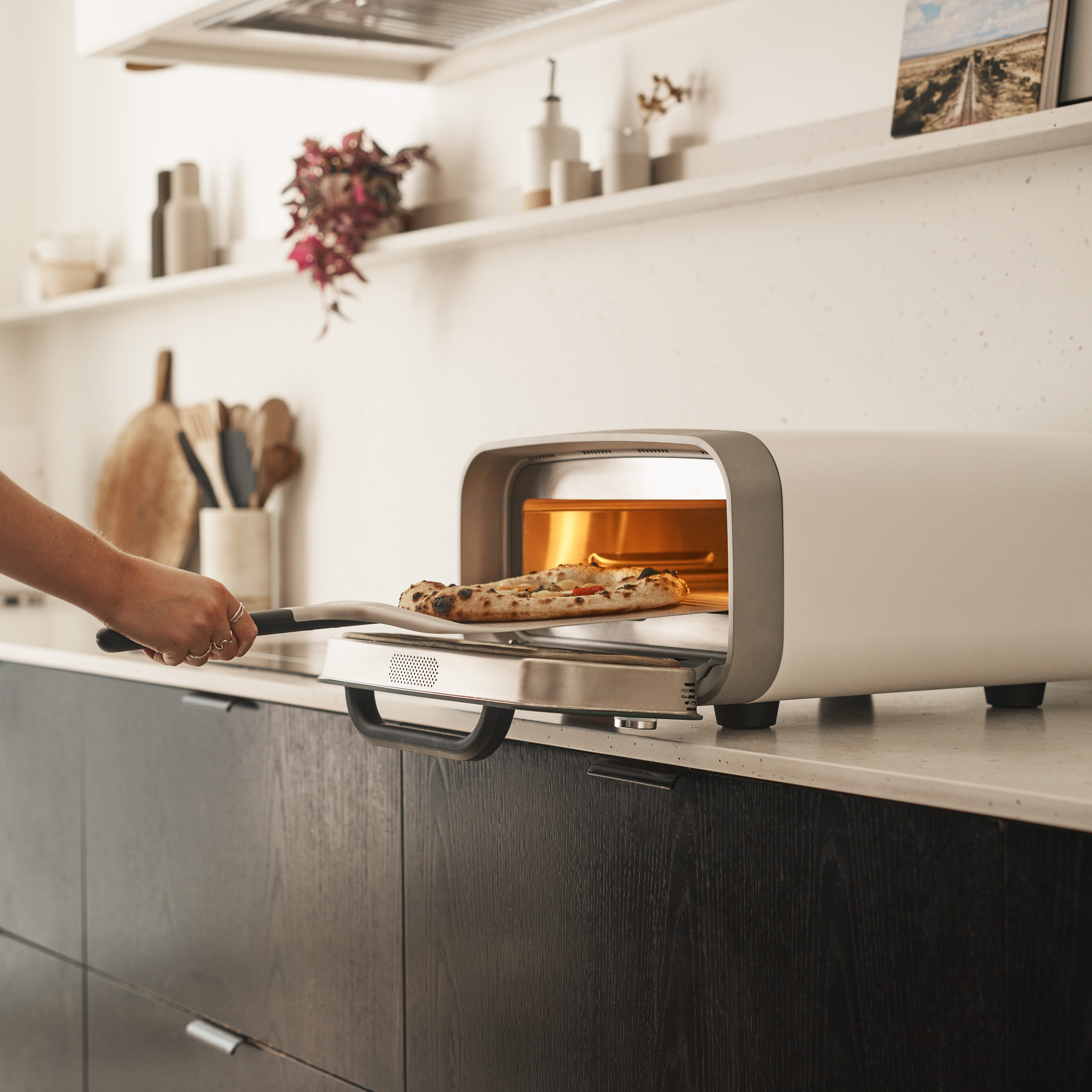 Person taking a pizza out of the White Ooni Volt 2 Pizza Oven.