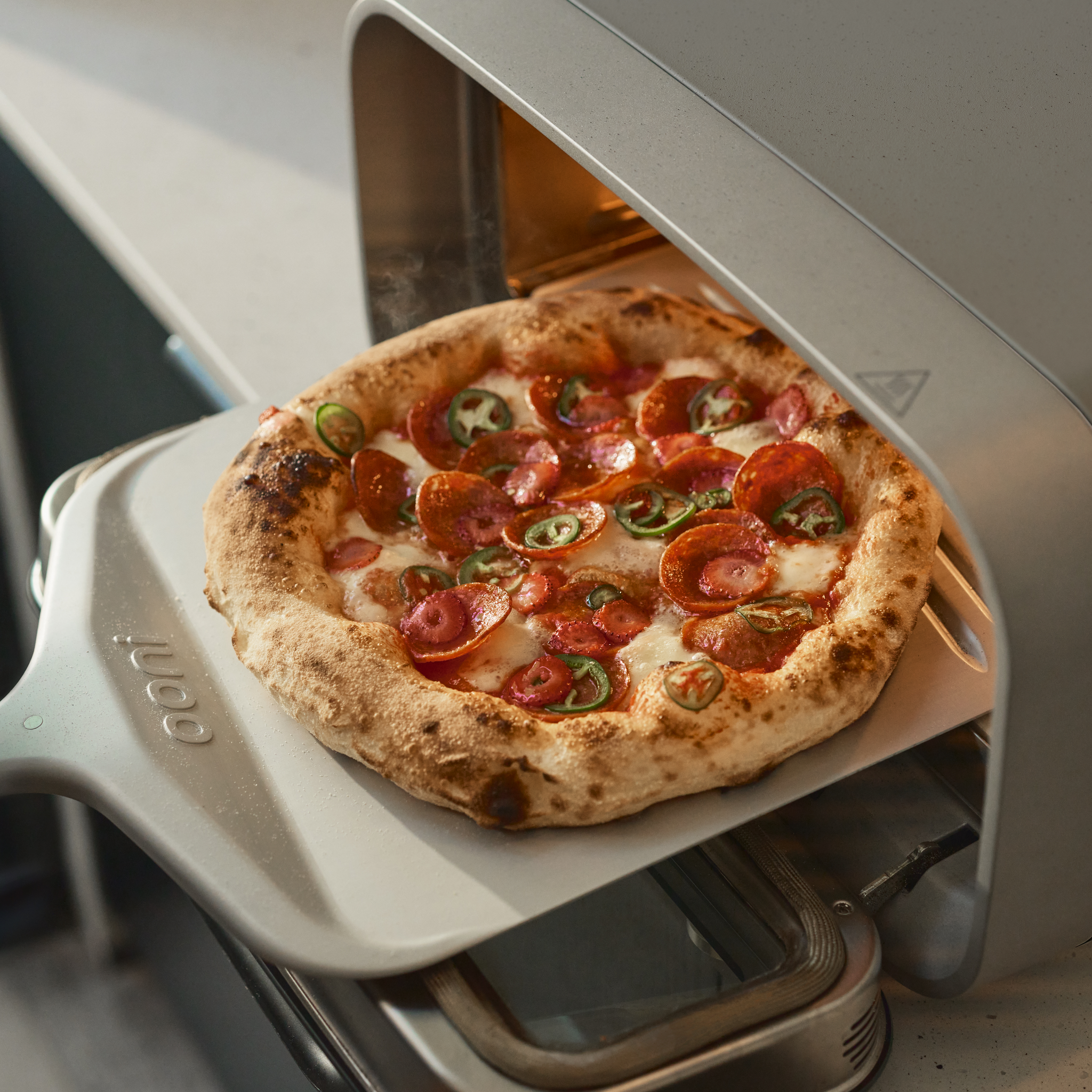Pizza with pepperoni and jalapeños being taken out of an Ooni Volt 2 Pizza Oven.