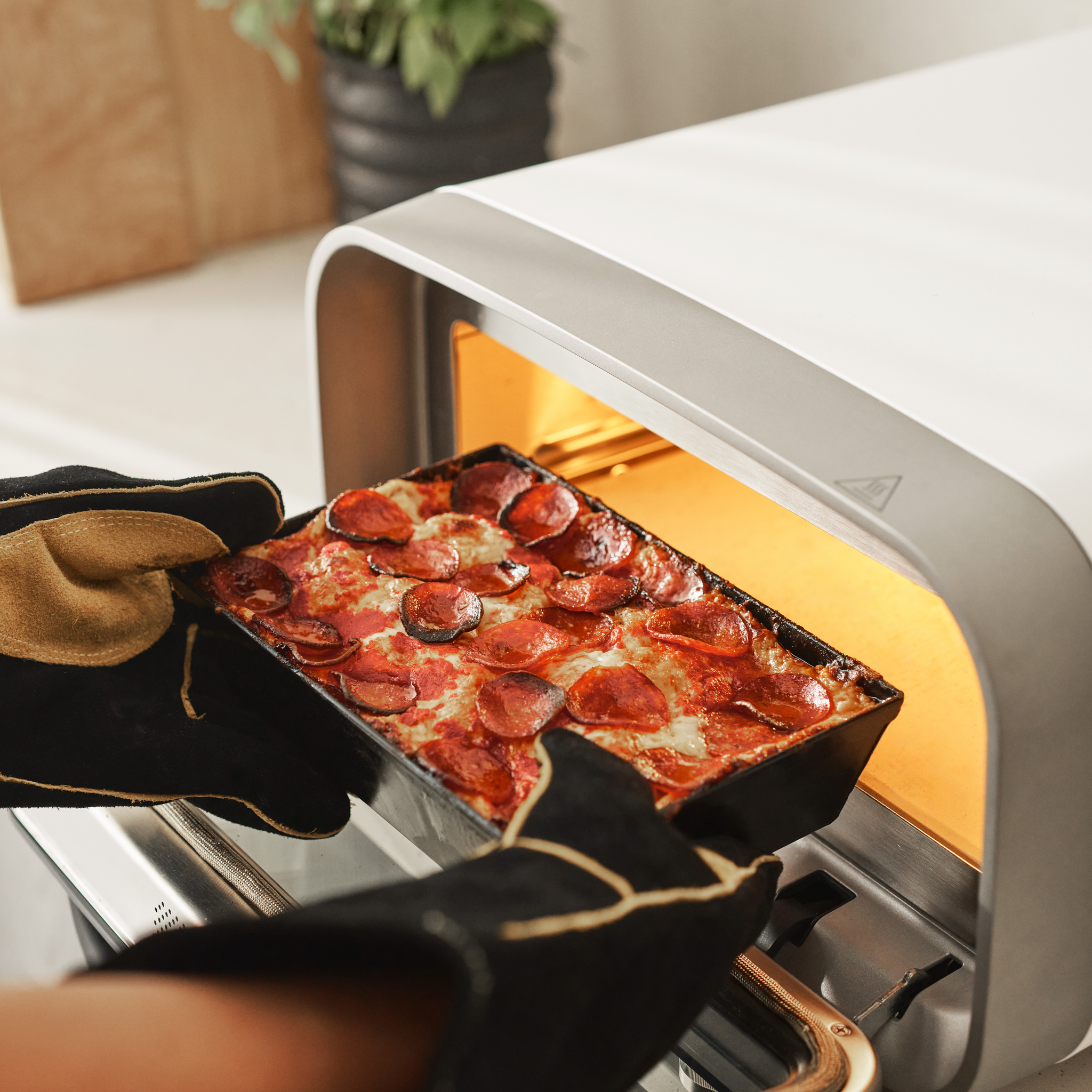 Person removing a Detroit pizza from the Ooni Volt 2 Pizza Oven.